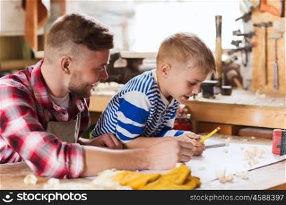 family, carpentry, woodwork and people concept - happy father and little son with blueprint at workshop