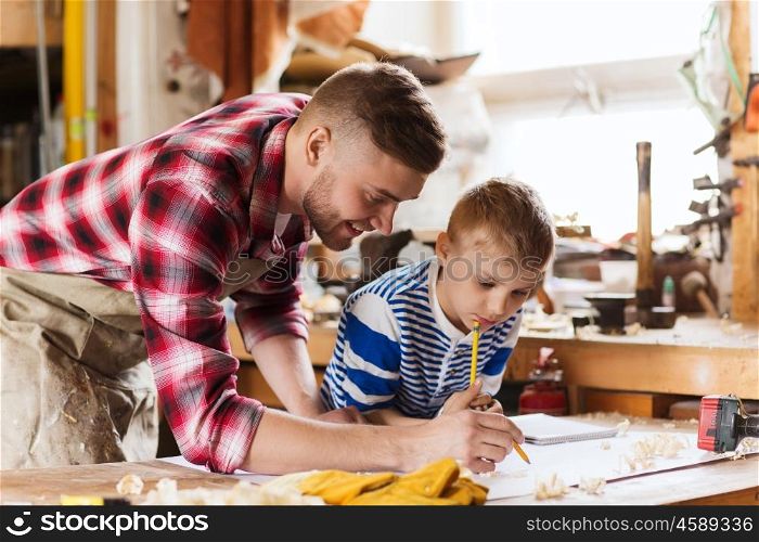 family, carpentry, woodwork and people concept - happy father and little son with blueprint at workshop