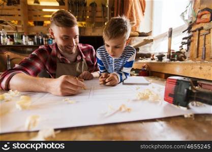 family, carpentry, woodwork and people concept - happy father and little son with blueprint at workshop. happy father and son with blueprint at workshop