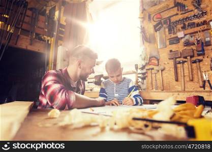 family, carpentry, woodwork and people concept - happy father and little son with blueprint at workshop. happy father and son with blueprint at workshop. happy father and son with blueprint at workshop