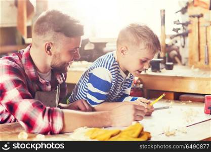 family, carpentry, woodwork and people concept - happy father and little son with blueprint at workshop. happy father and son with blueprint at workshop. happy father and son with blueprint at workshop