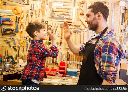 family, carpentry, woodwork, gesture and people concept - happy father and little son making high five at workshop