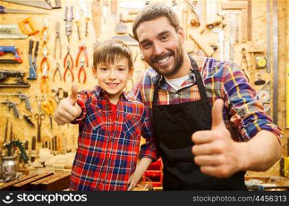 family, carpentry, woodwork, gesture and people concept - happy father and little son making thumbs up at workshop