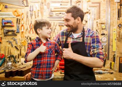 family, carpentry, woodwork, gesture and people concept - happy father and little son making thumbs up at workshop