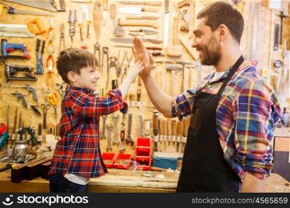 family, carpentry, woodwork, gesture and people concept - happy father and little son making high five at workshop