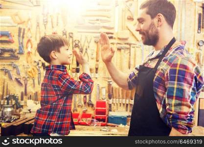 family, carpentry, woodwork, gesture and people concept - happy father and little son making high five at workshop. father and little son making high five at workshop