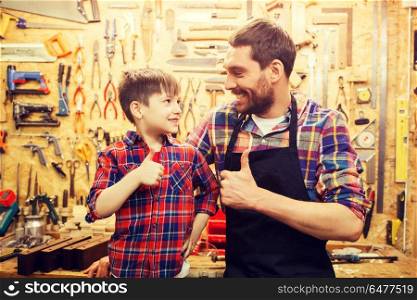 family, carpentry, woodwork, gesture and people concept - happy father and little son making thumbs up at workshop. father and little son making thumbs up at workshop. father and little son making thumbs up at workshop