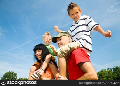 Family carrying their two kids piggyback under a perfect blue sky