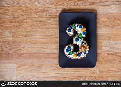 family celebration with a cake in the form of number three with place for text on wooden table. family celebration with a cake in the form of number three. Top view