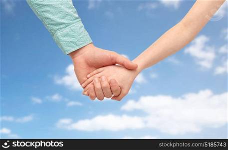 family, charity, care and people concept - happy father and child holding hands over blue sky and clouds background. happy father and child holding hands