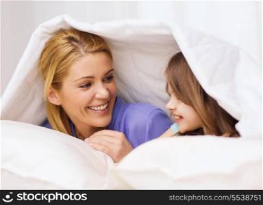 family, child and home concept - smiling mother and little girl under blanket at home