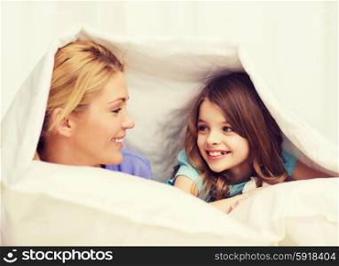 family, child and home concept - smiling mother and little girl under blanket at home