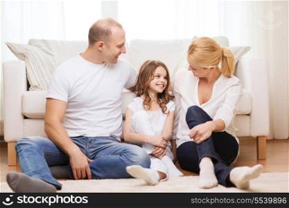 family, child and home concept - smiling parents and little girl sitting on floor at home