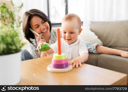 family, child and motherhood concept - happy baby boy playing developmental toy and mother calling on smartphone at home. baby boy playing toy and mother calling on phone