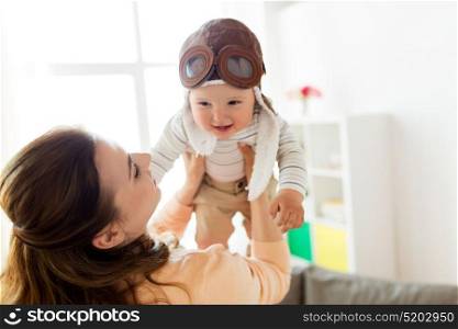 family, child and motherhood concept - happy smiling young mother playing with little baby wearing pilot hat at home (focus on mother). happy mother with baby wearing pilot hat at home
