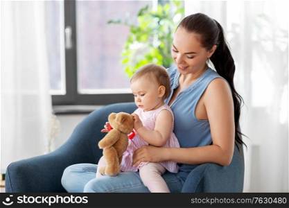 family, child and motherhood concept - portrait of happy smiling mother and little baby daughter with teddy bear toy sitting in chair at home. happy mother with little baby daughter at home