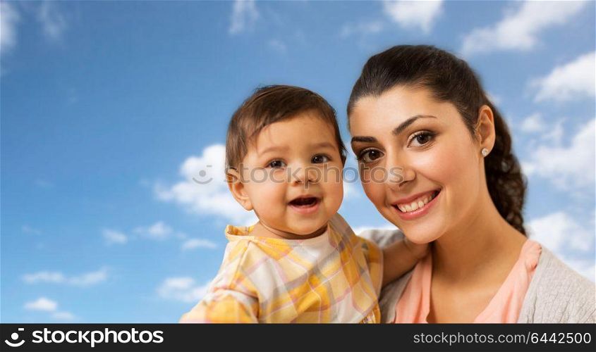 family, child and motherhood concept - portrait of happy smiling mother with little baby daughter over blue sky and clouds background. portrait of happy mother with baby daughter