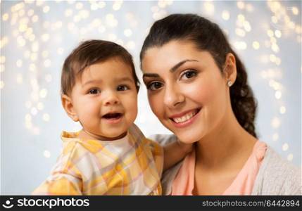 family, child and motherhood concept - portrait of happy smiling mother with little baby daughter over holidays lights background. portrait of happy mother with baby daughter