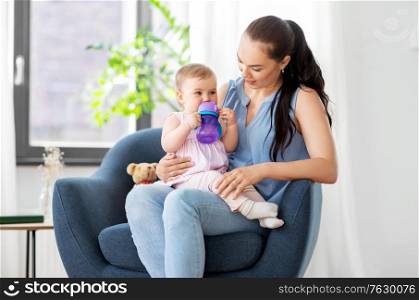 family, child and motherhood concept - portrait of happy smiling mother with little baby daughter drinking from bottle at home. happy mother with little baby daughter at home