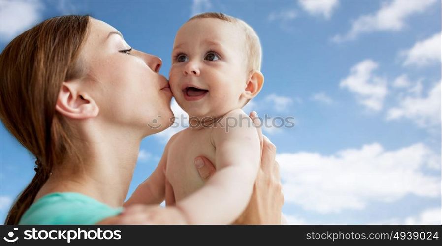family, child and parenthood concept - close up of happy smiling young mother kissing little baby over blue sky and clouds background. happy mother kissing little baby over blue sky