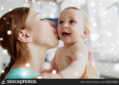 family, child and parenthood concept - close up of happy smiling young mother kissing little baby at home over snow. happy young mother kissing little baby at home