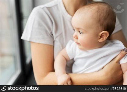 family, child and parenthood concept - close up of young mother holding little baby daughter over grey background. close up of mother holding little baby daughter