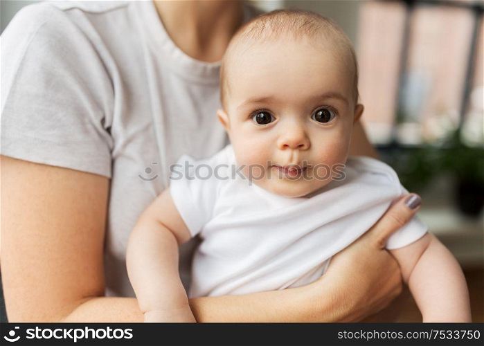 family, child and parenthood concept - close up of young mother holding little baby daughter over grey background. close up of mother holding little baby daughter