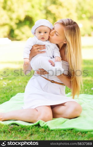 family, child and parenthood concept - happy mother kissing her little baby and sitting on blanket in park