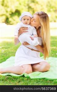 family, child and parenthood concept - happy mother kissing her little baby and sitting on blanket in park