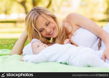 family, child and parenthood concept - happy mother lying with little baby on blanket in park