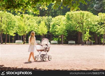 family, child and parenthood concept - happy mother walking with baby stroller in park from back