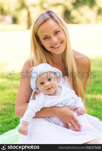 family, child and parenthood concept - happy mother with little baby sitting on blanket in park