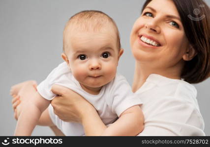 family, child and parenthood concept - happy smiling middle-aged mother holding little baby daughter over grey background. happy middle-aged mother with little baby daughter