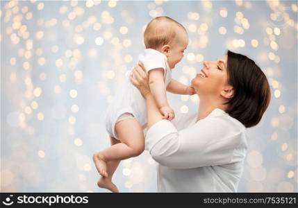 family, child and parenthood concept - happy smiling middle-aged mother holding little baby daughter over festive lights background. happy middle-aged mother with little baby daughter