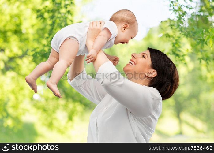 family, child and parenthood concept - happy smiling middle-aged mother holding little baby daughter over green natural background. happy middle-aged mother with little baby daughter