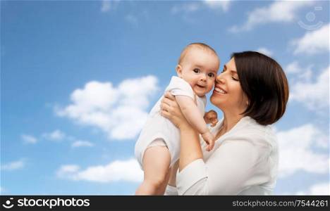 family, child and parenthood concept - happy smiling middle-aged mother holding little baby daughter over blue sky and clouds background. happy middle-aged mother with little baby daughter