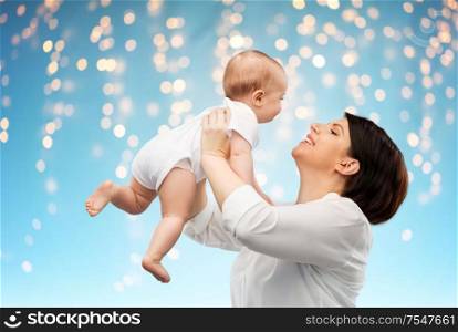 family, child and parenthood concept - happy smiling middle-aged mother holding little baby daughter over lights on blue background. happy middle-aged mother with little baby daughter