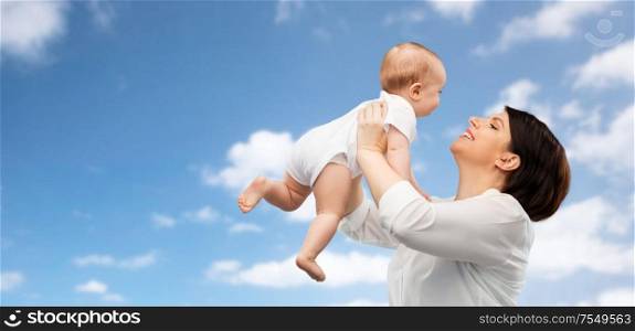 family, child and parenthood concept - happy smiling middle-aged mother holding little baby daughter over blue sky and clouds background. happy middle-aged mother with little baby daughter