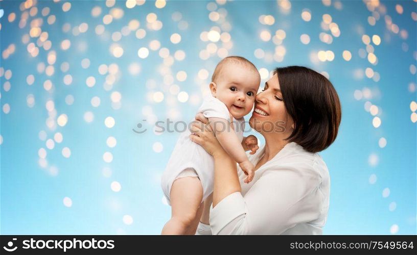 family, child and parenthood concept - happy smiling middle-aged mother holding little baby daughter over lights on blue background. happy middle-aged mother with little baby daughter
