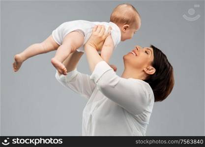 family, child and parenthood concept - happy smiling middle-aged mother holding little baby daughter over grey background. happy middle-aged mother with little baby daughter