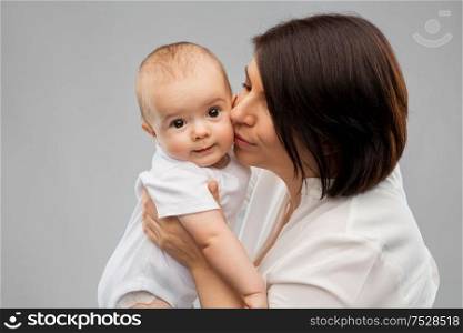 family, child and parenthood concept - happy smiling middle-aged mother kissing little baby daughter over grey background. happy mother kissing little baby daughter
