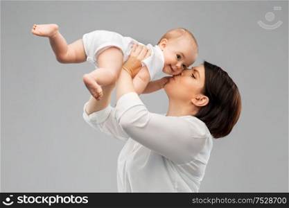 family, child and parenthood concept - happy smiling middle-aged mother kissing little baby daughter over grey background. happy mother kissing little baby daughter