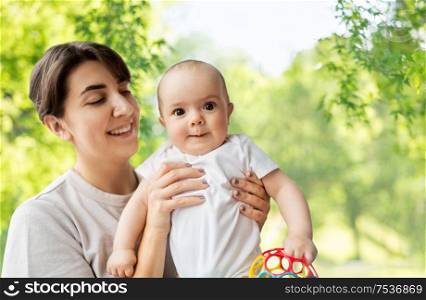 family, child and parenthood concept - happy smiling young mother holding little baby daughter over green natural background. happy young mother holding little baby daughter
