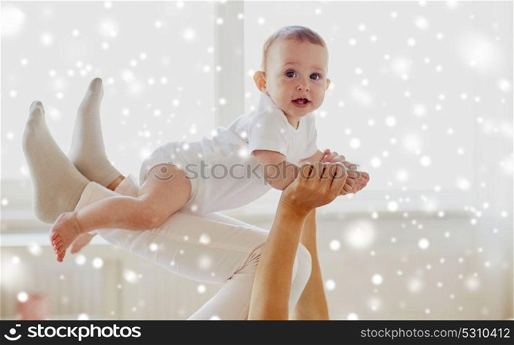 family, child and parenthood concept - happy smiling young mother playing with little baby at home over snow. happy mother playing with baby at home