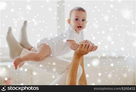 family, child and parenthood concept - happy smiling young mother playing with little baby at home over snow. happy mother playing with baby at home