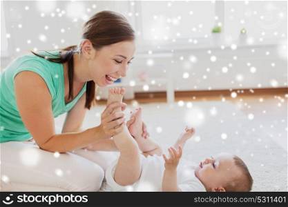 family, child and parenthood concept - happy smiling young mother playing with little baby or doing gymnastics exercise for toddlers at home over snow. happy mother playing with little baby at home
