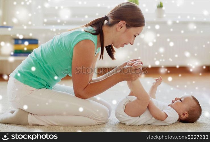 family, child and parenthood concept - happy smiling young mother playing with little baby or doing gymnastics exercise for toddlers at home over snow. happy mother playing with little baby at home