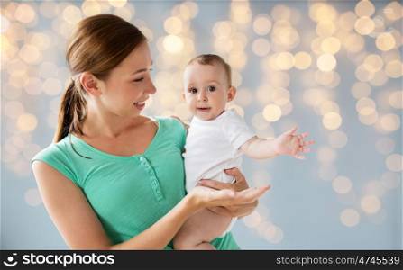 family, child and parenthood concept - happy smiling young mother with little baby over holidays lights background