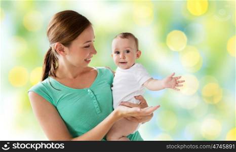 family, child and parenthood concept - happy smiling young mother with little baby over green holidays lights background