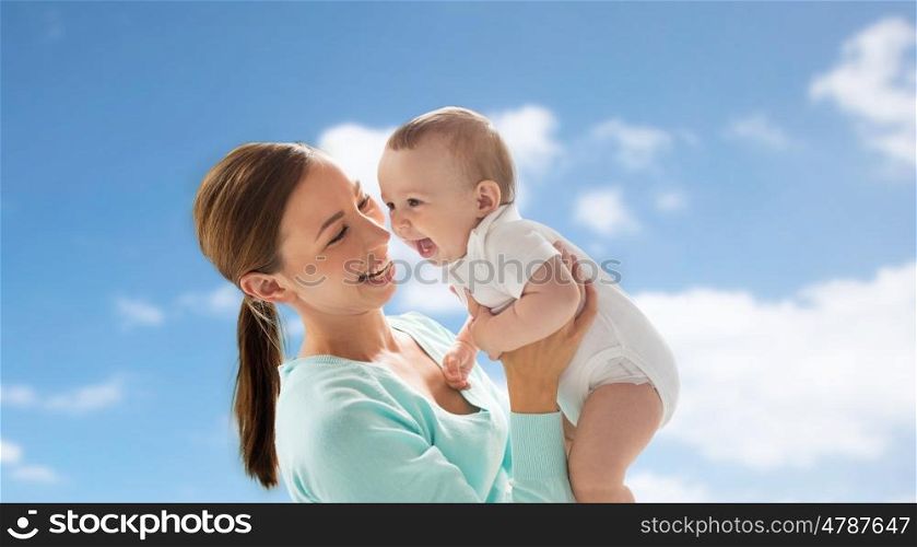 family, child and parenthood concept - happy smiling young mother with little baby over blue sky and clouds background